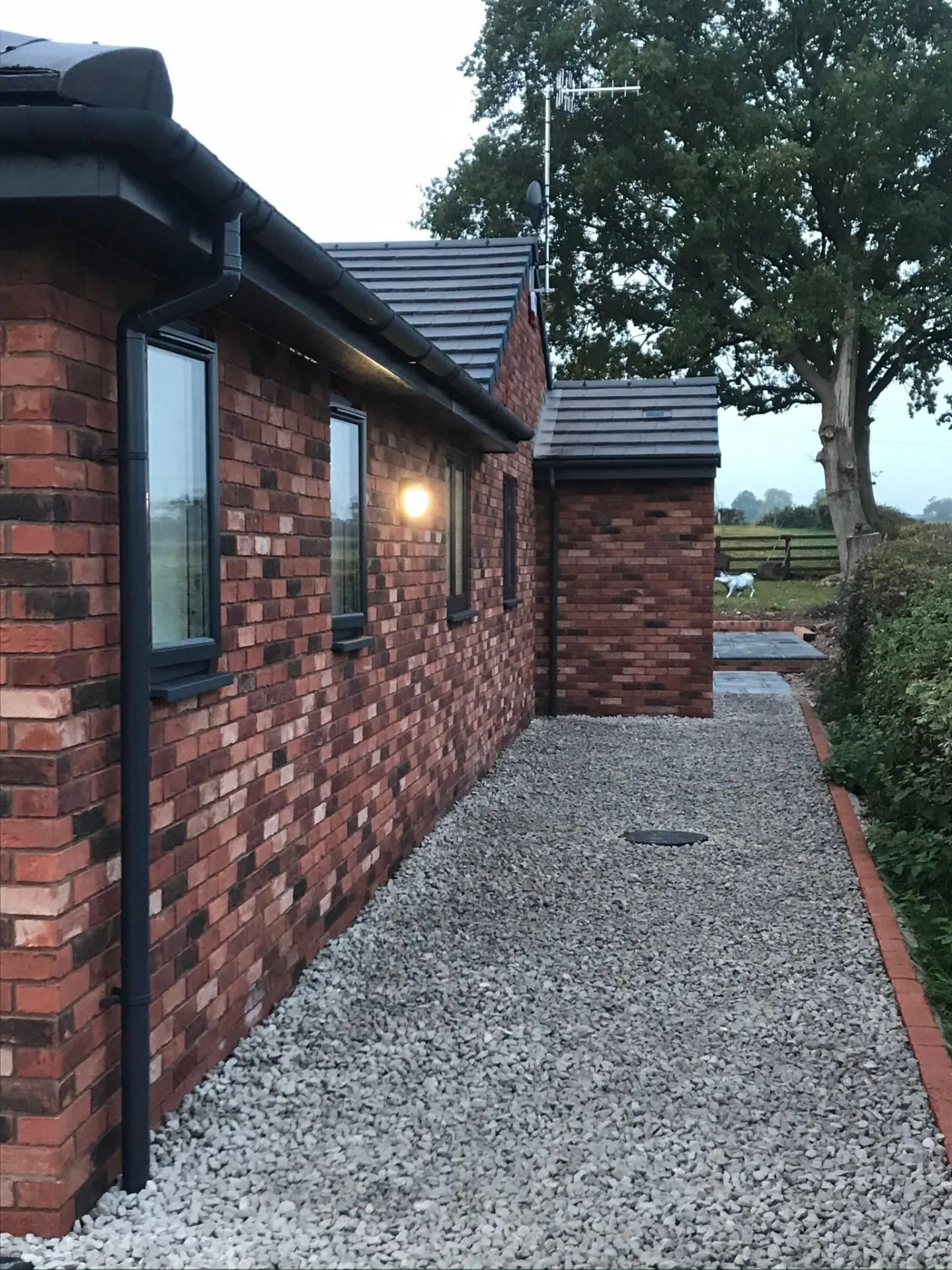 Reclaimed-blend brickwork elevation of a new-build bungalow with anthracite windows, a white gravel margin and brick-edged path alongside