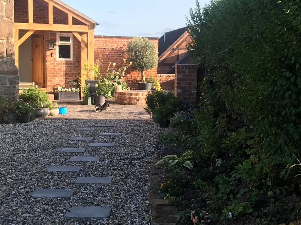 Evening view of the restored farmhouse courtyard with oak porch, brick walls, olive tree and planted borders