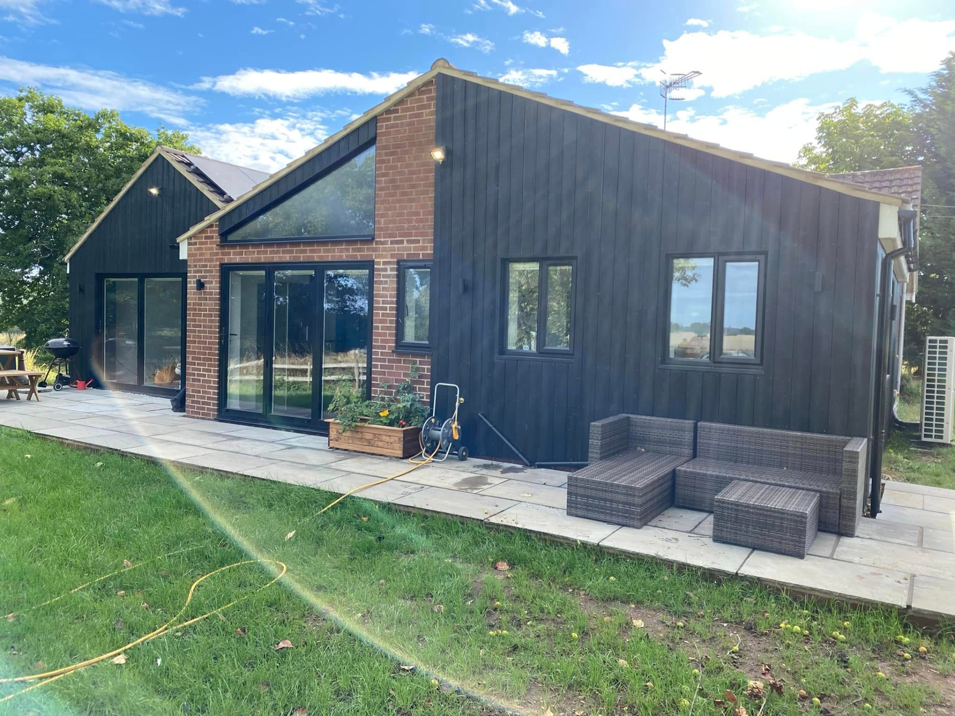 Rear elevation of the kitchen, utility and dining extension showing brick and black clad gables and a wide sandstone terrace