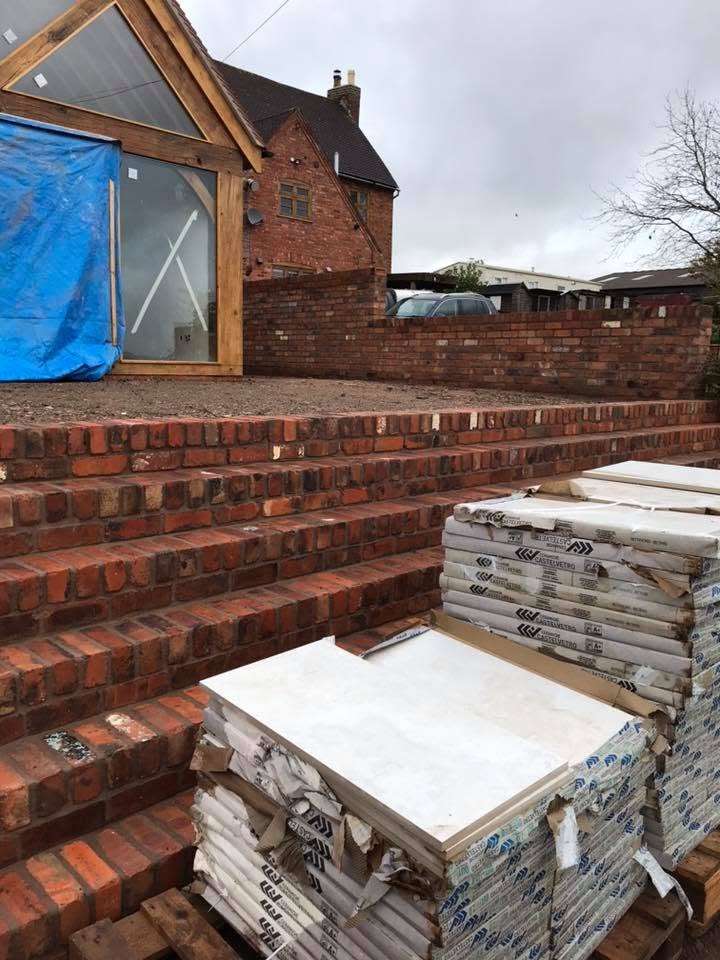 New hand-laid reclaimed brick garden steps and retaining walls under construction at the Grade II listed farmhouse, with porcelain paving stacked ready to lay