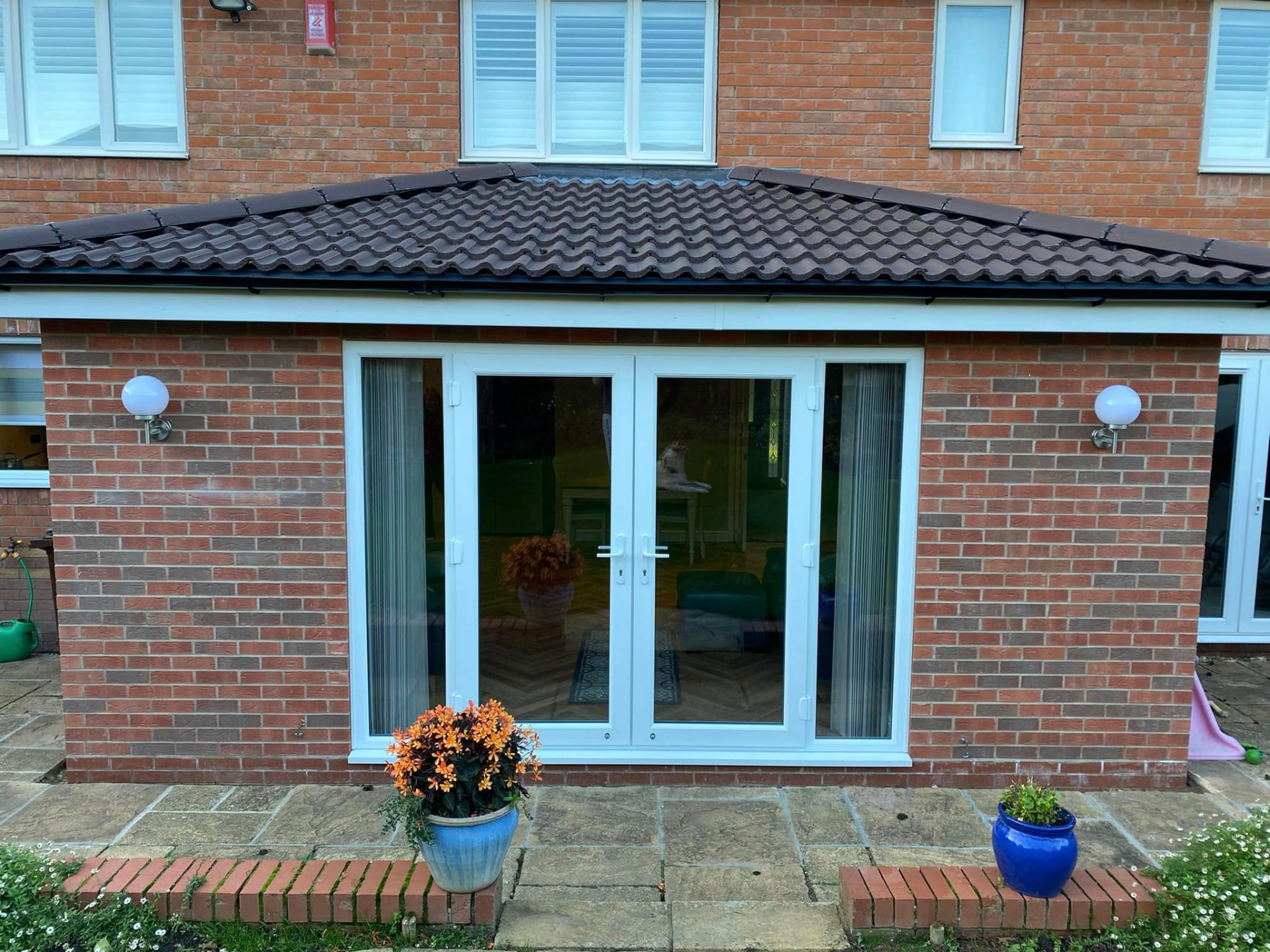 Close view of the brick extension elevation with white French doors, wall lights and re-laid sandstone patio and brick edging