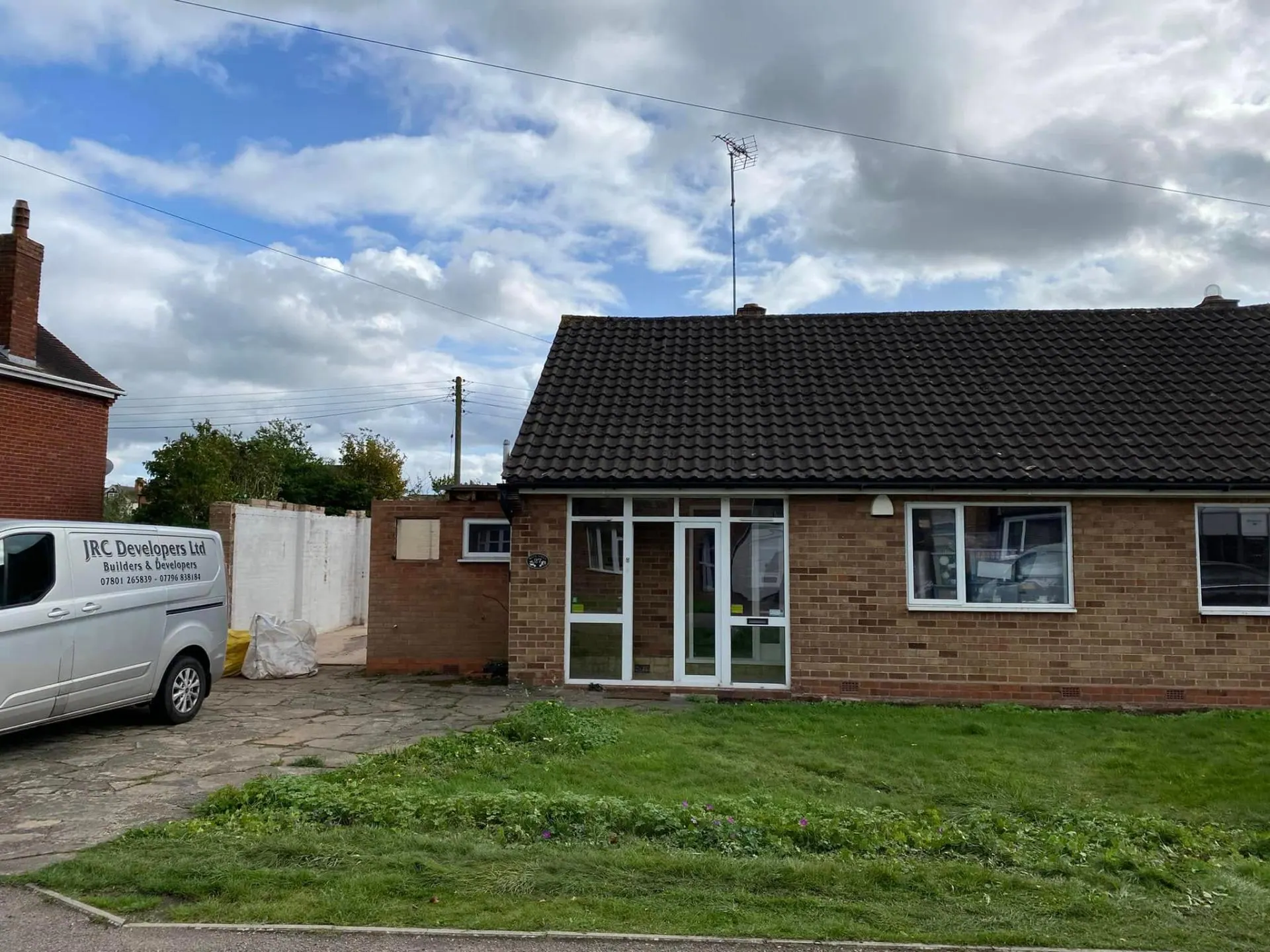 Original front elevation of the White Gates bungalow on day one with the JRC Developers Ltd van parked outside — dated brick porch, black concrete tile roof and tired garden