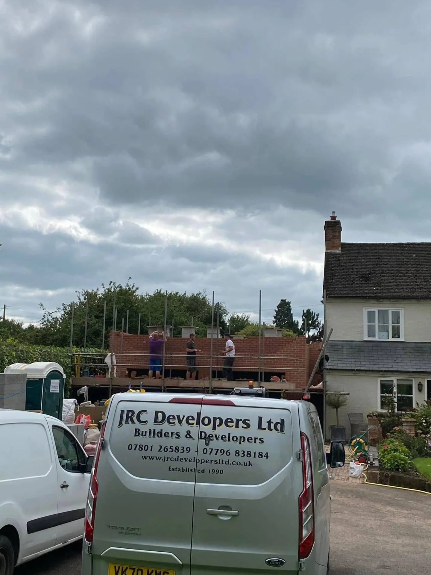 JRC Developers crew building first-floor brickwork on scaffold with the JRC Ford Transit van in the yard