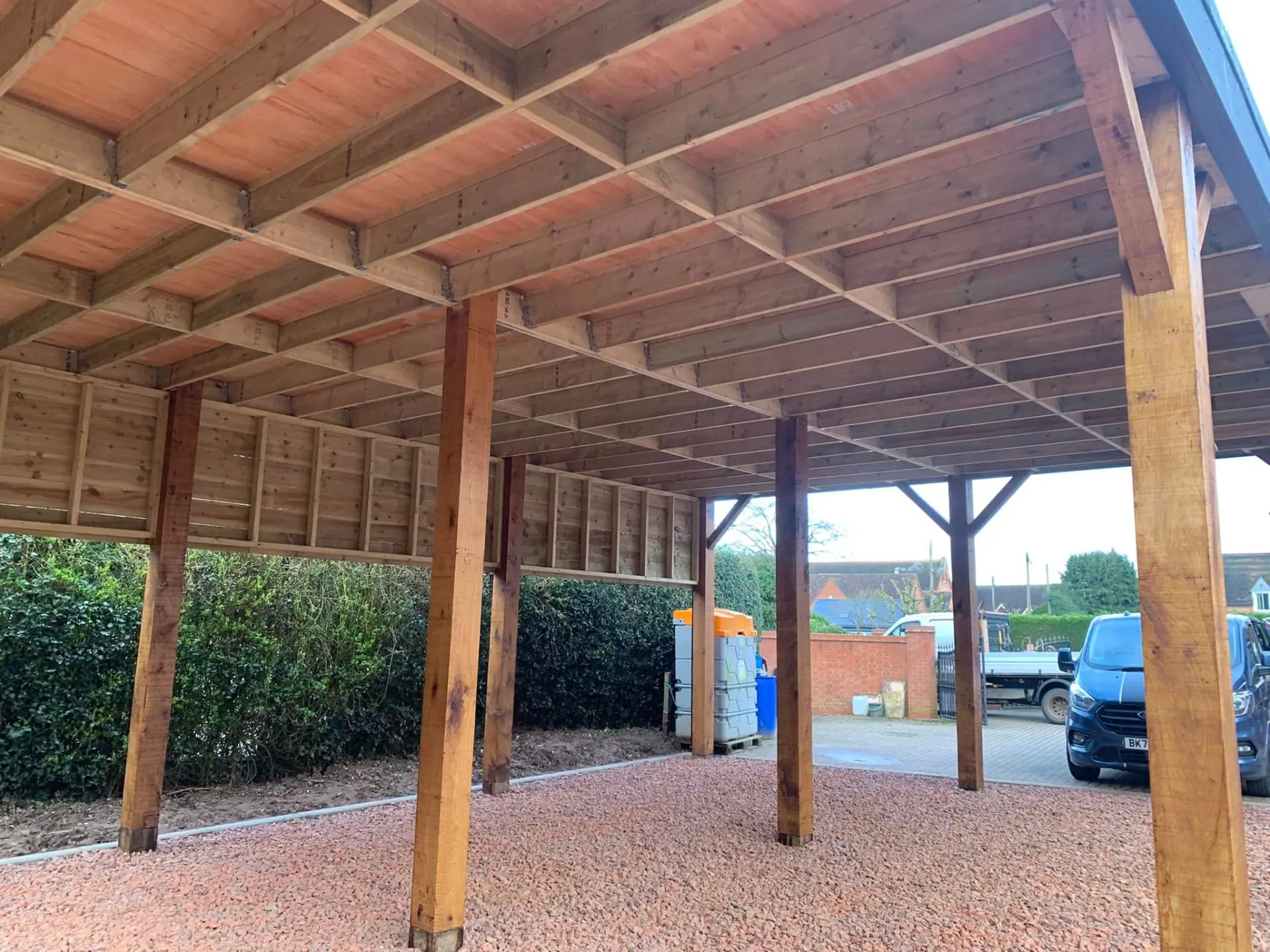 Underside of the oak tractor port roof structure showing timber joists, rafters and the boarded rear wall