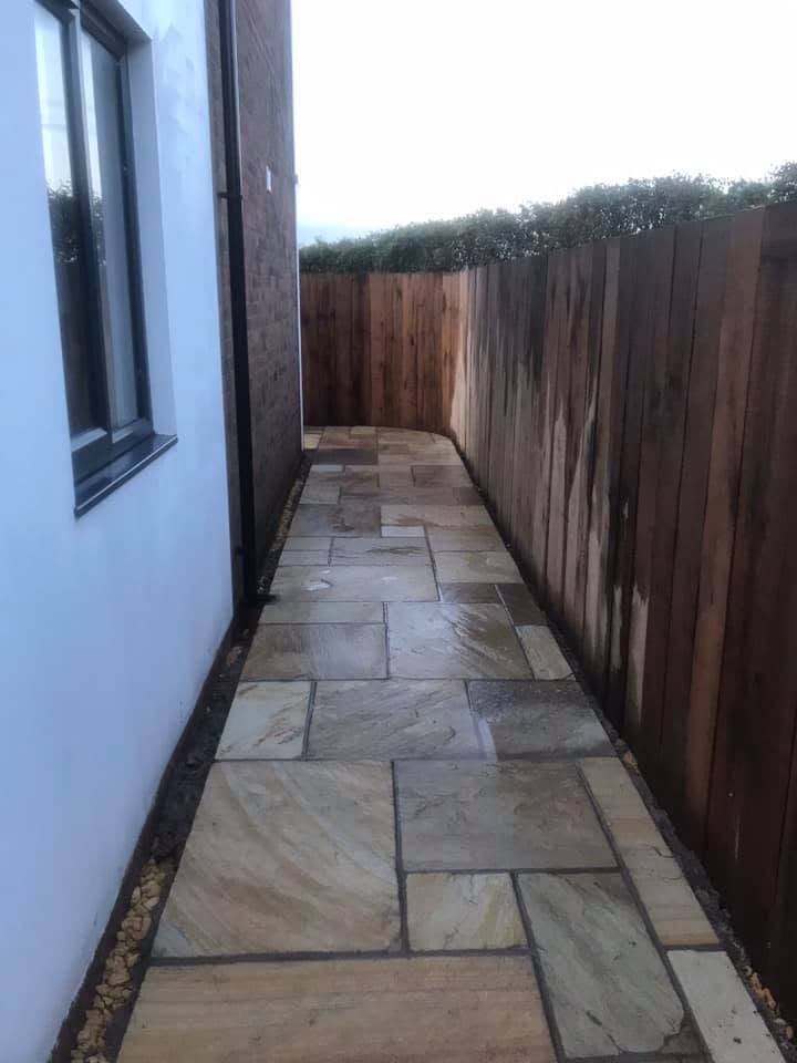 Indian sandstone side path running between a white rendered elevation and a close-board timber fence