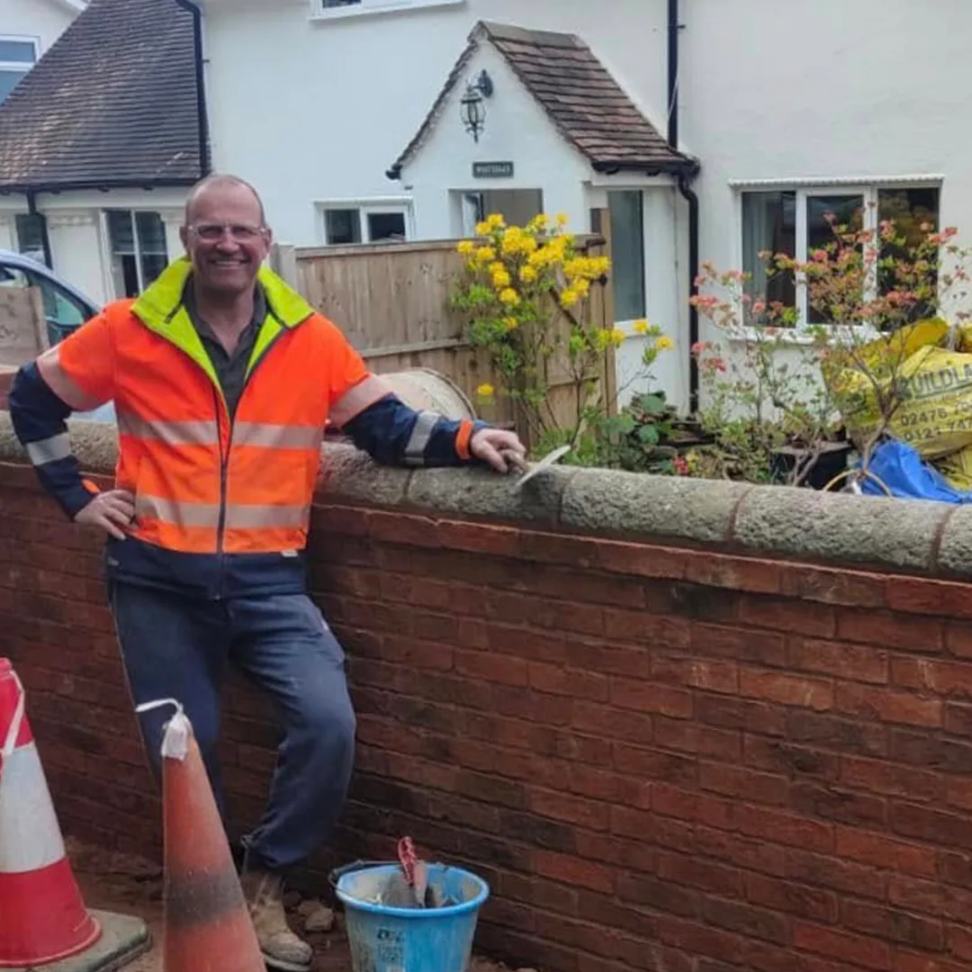 John in hi-vis beside a newly built red brick garden wall