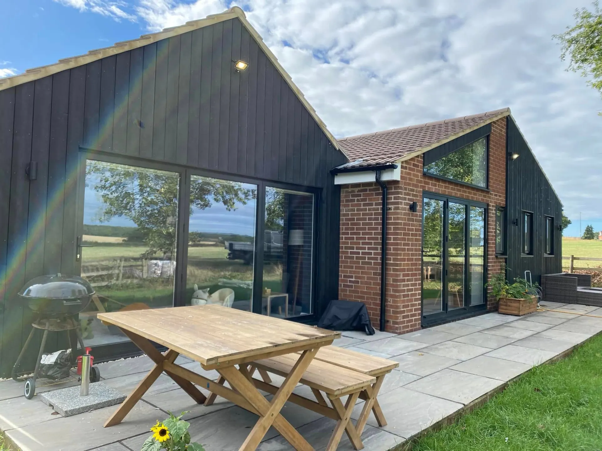 Finished kitchen, utility and dining room extension with black timber cladding, brick gable, aluminium sliding doors and Indian sandstone patio in rural Worcestershire