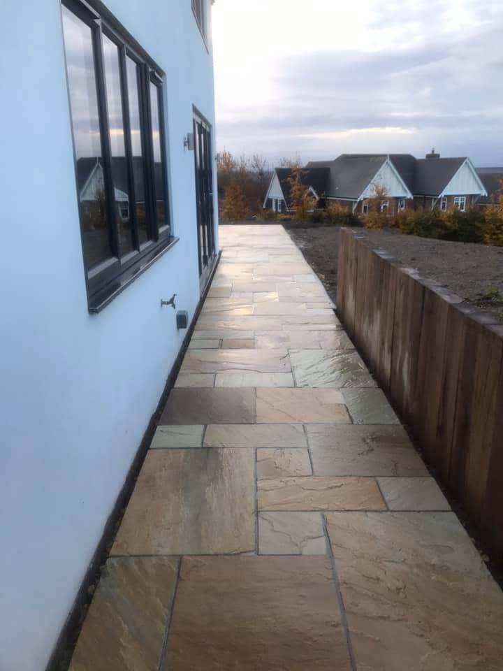 Indian sandstone path alongside a rendered house with a timber sleeper retaining wall and open countryside beyond