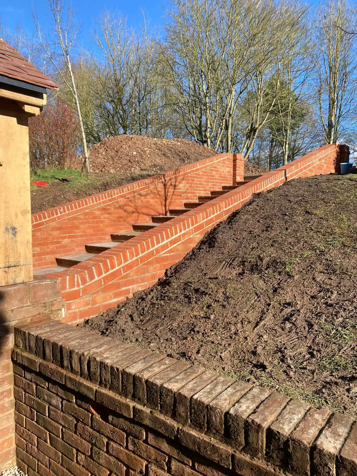 Diagonal view of the new brick steps and retaining walls rising up the bank beside the oak porch