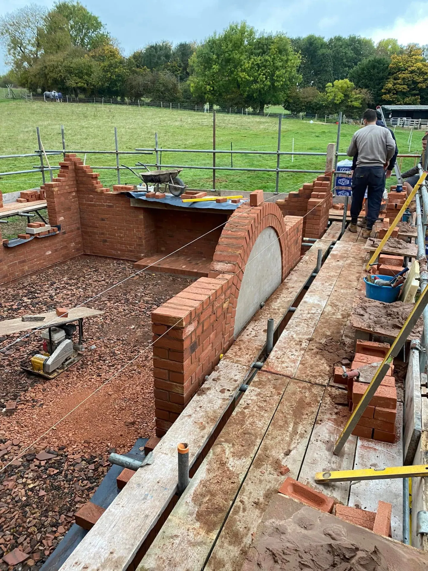 Brick arch doorway of the man cave under construction with scaffold boards, string lines and open Worcestershire fields behind