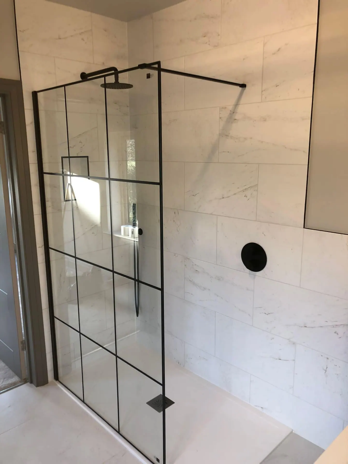 Walk-in shower with black-framed glazing and marble-effect wall tiles in the finished Wootton Mead bathroom